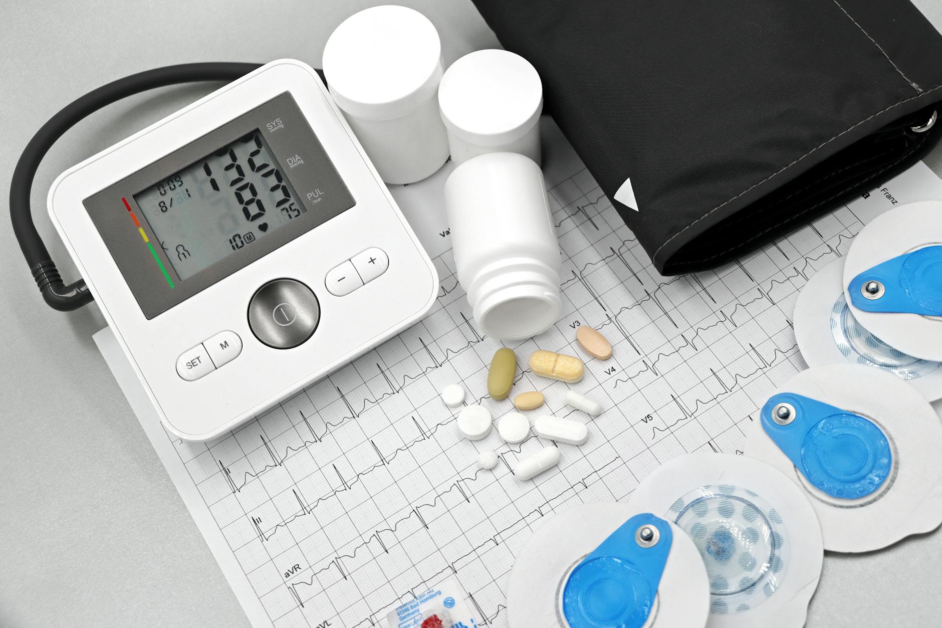 Flat lay of blood pressure monitor, pills, and ECG printout for heart health theme.