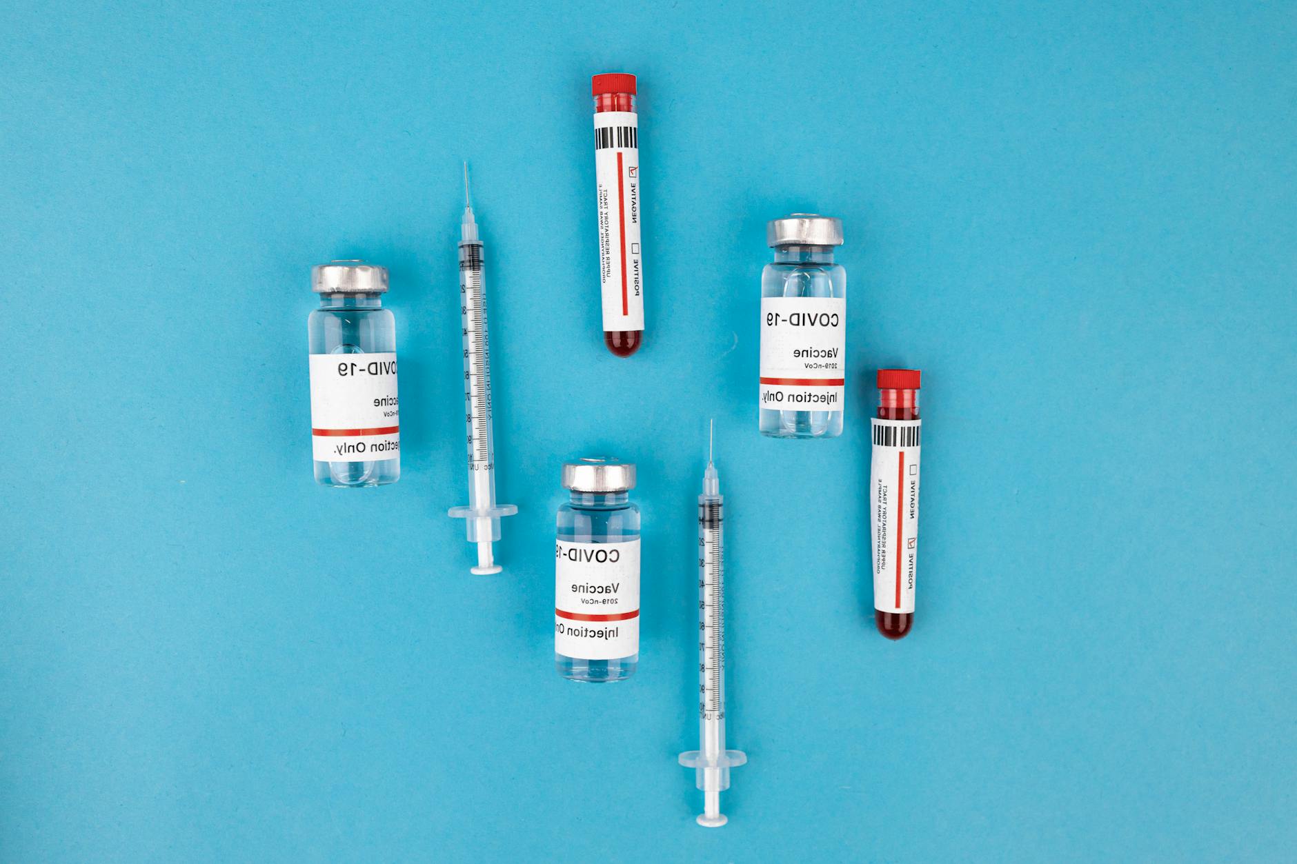 Top view of COVID-19 vaccine vials, syringes, and test tubes on a blue background, representing immunization and protection.